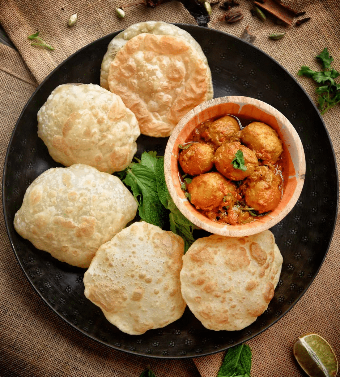 A plate of five fluffy luchis paired with flavourful dum aloo beautifully garnished with a sprinkle of spices