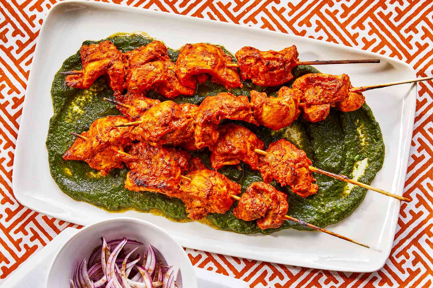 Chicken tikka kebab placed on green chutney s spread served with masala onion