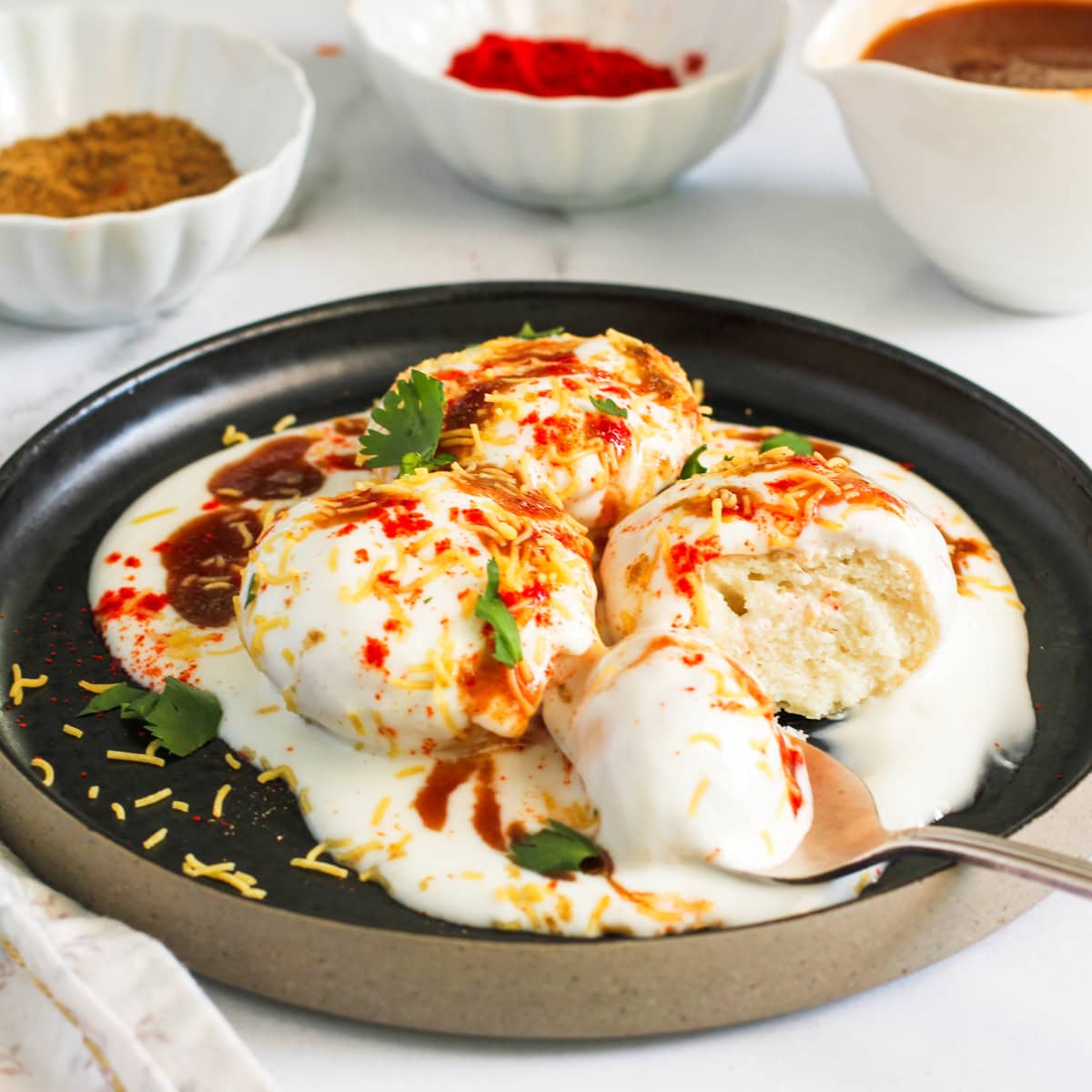 Dahi vada ready to be served in a black quarter plate garnished with masala and cilantro