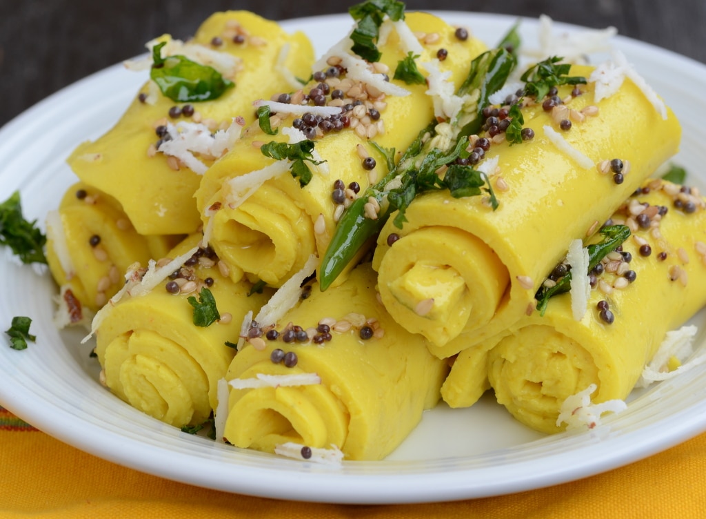 Khandvi set in a plate with green chili and seeds spread on top