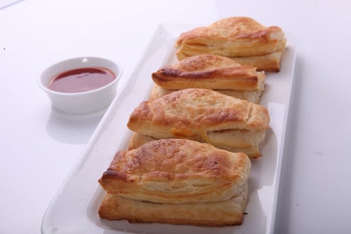 Paneer puffs lined on a long white tray with sauce in a bowl by its side