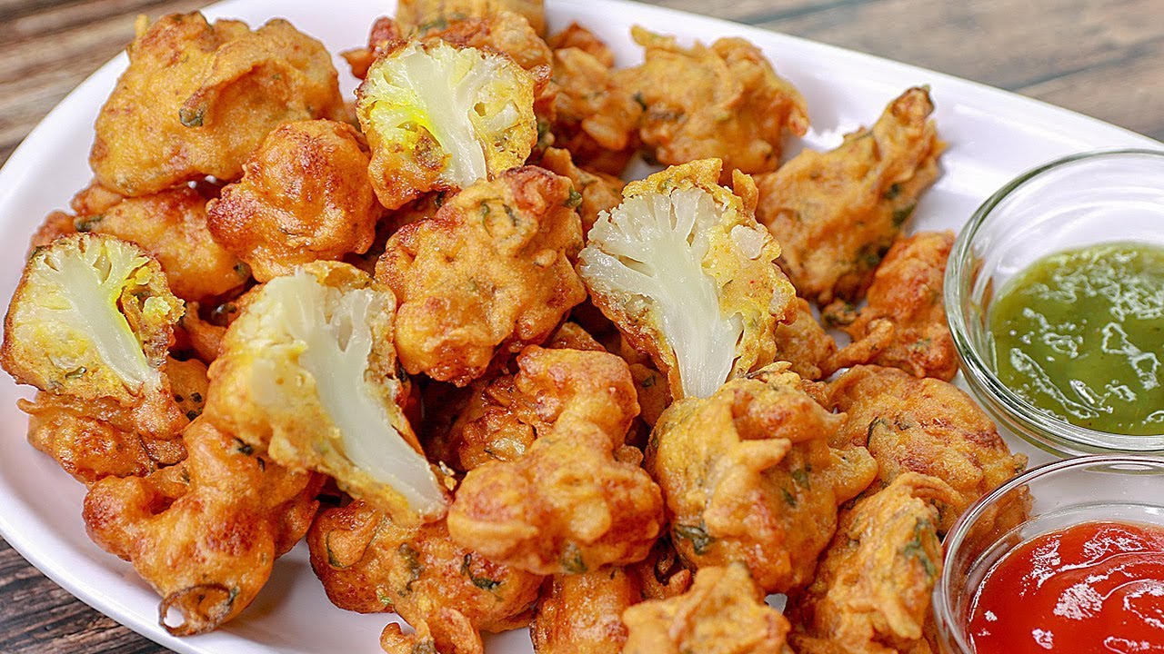 Plate full of gobi pakora served with green chutney and sauce