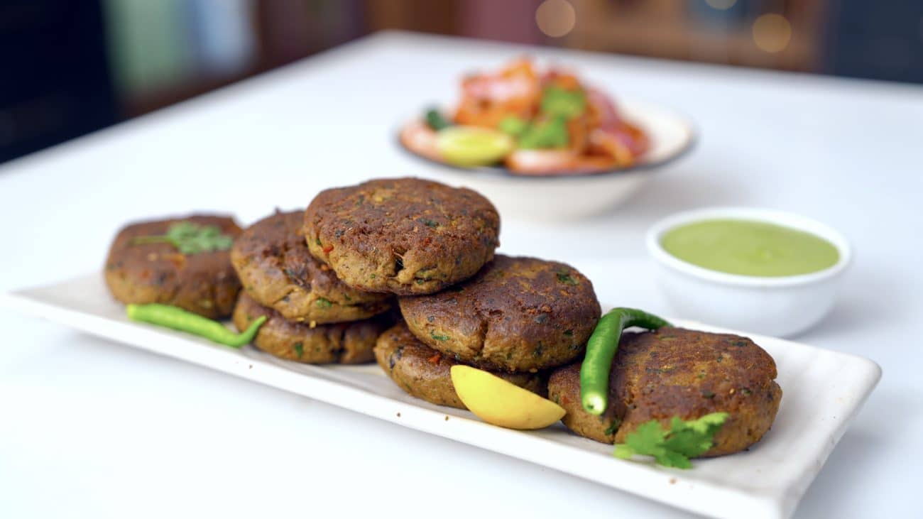 Shami kebab stacked on long white tray to be served with green chutney