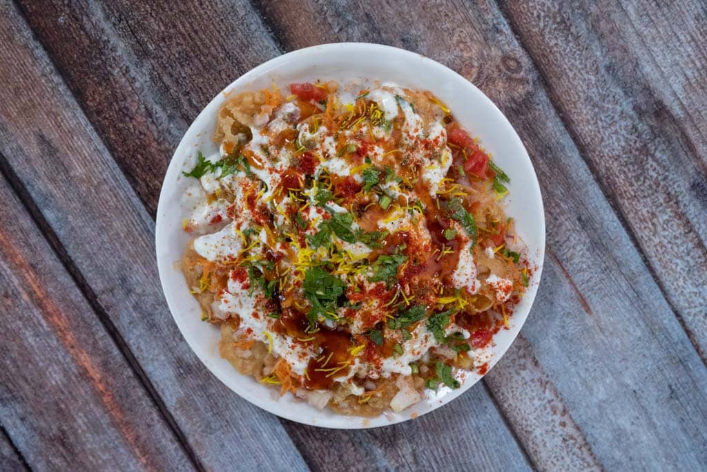 White plate filled with papdi chaat garnished with spices and seasoning