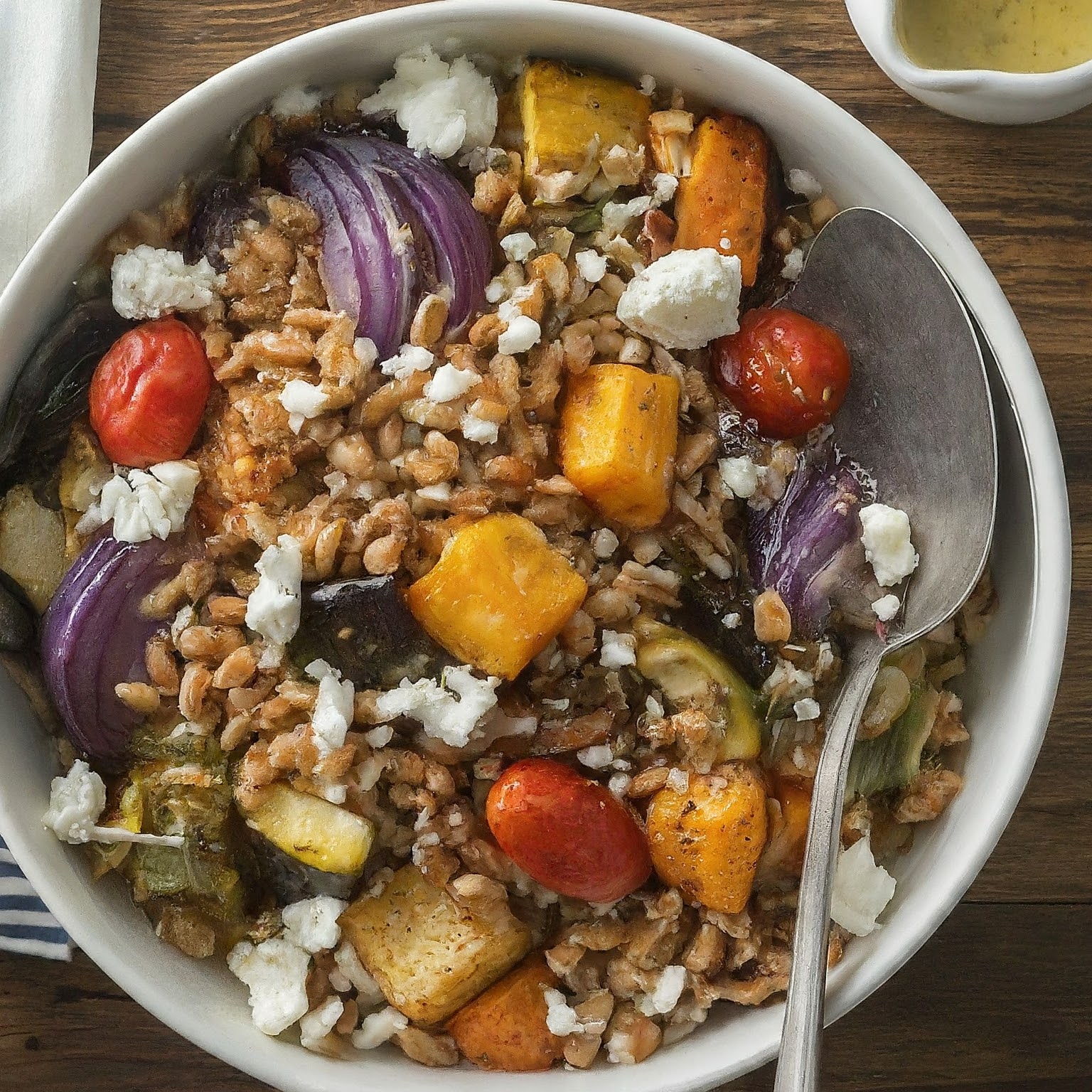 A colourful salad made with farro, roasted veggies, and grated cheese, served in a rustic bowl