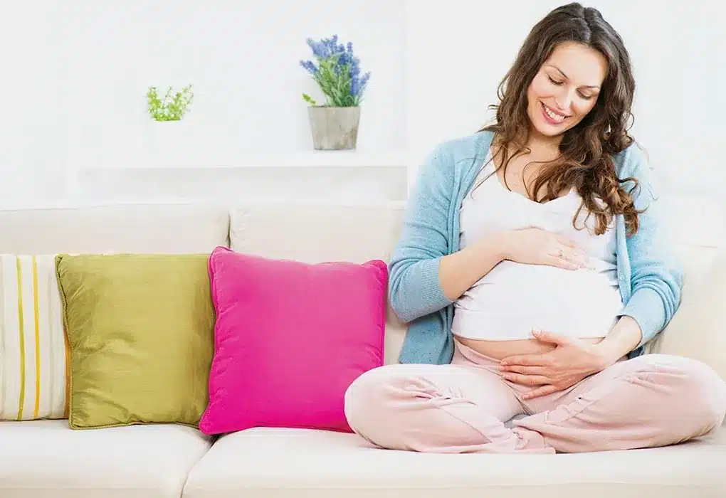 Smiling pregnant woman sitting on a sofa.