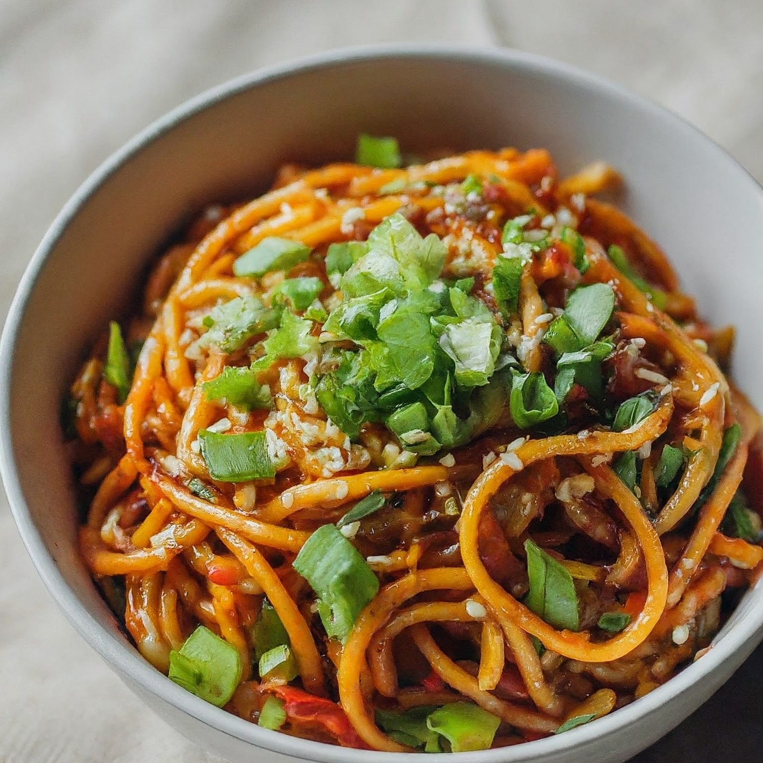 A plate of spicy vegetarian Schezwan Hakka noodles, tossed in a fiery red sauce with mixed vegetables.