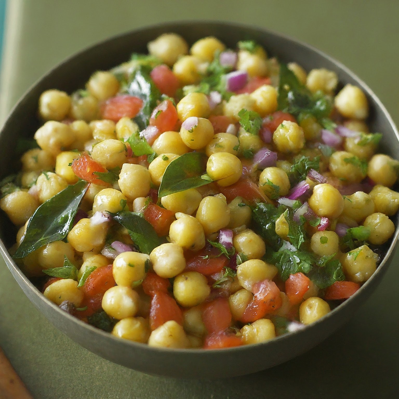 A bowl of chickpea salad with curry leaves.