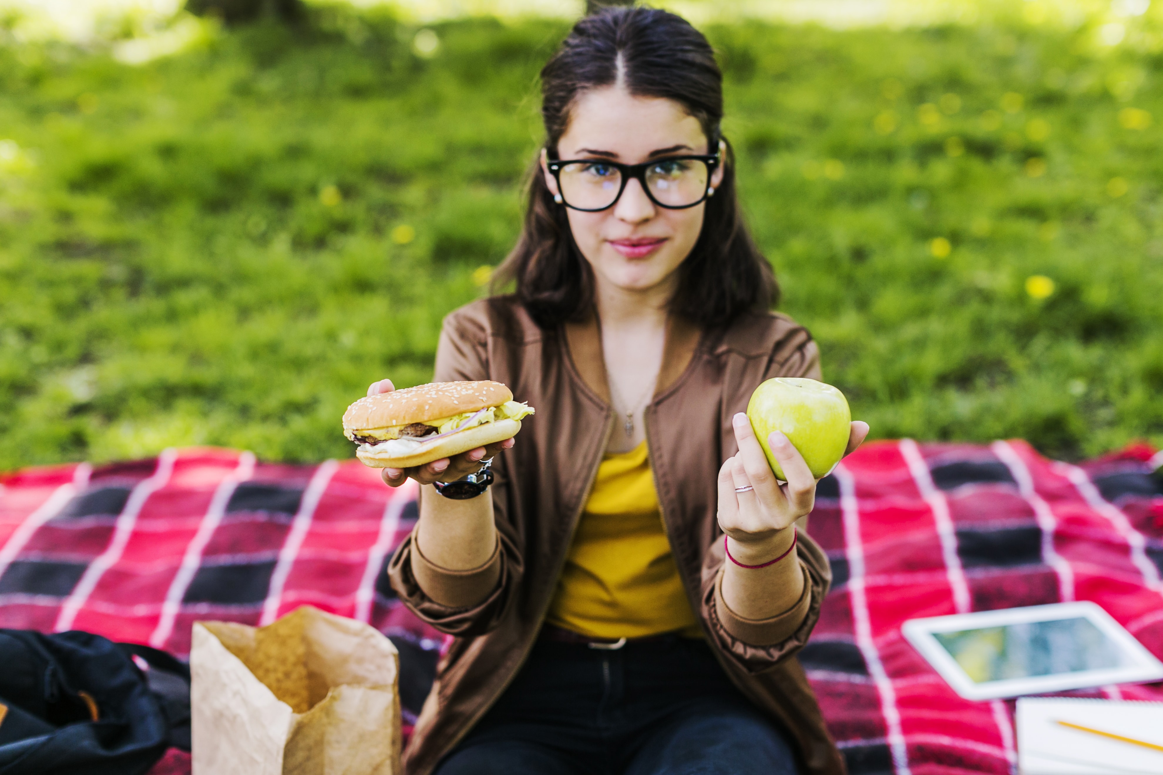 A woman holding a burger in one hand and an apple in the other