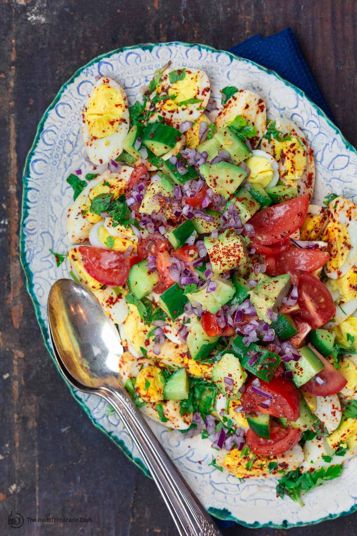 Egg Salad with diced Tomato and Cucumber in a bowl garnished with fresh coriander leaves on a wooden table 