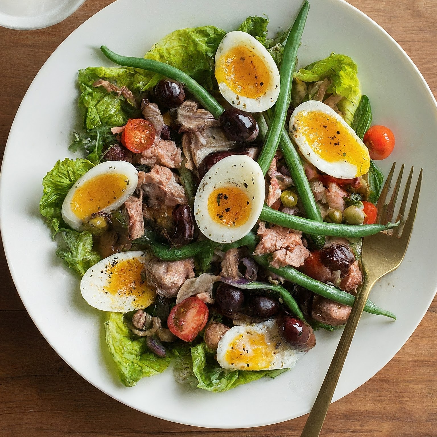 French Niçoise Salad is ready to eat and served on a white plate with a golden fork on the side