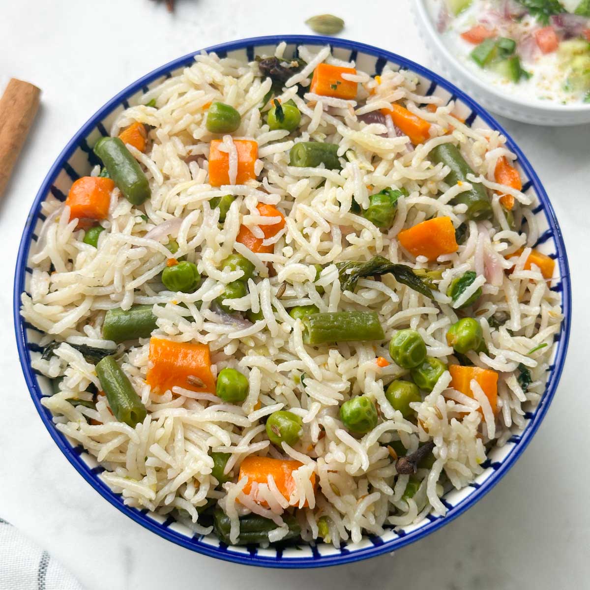 Freshly cooked vegetable pulao with different veggies and basmati rice in a blue-striped bowl.