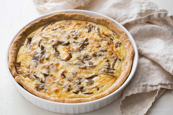 Golden brown Onion and Gruy re Quiche served on a wooden plate garnished with fresh herbs 