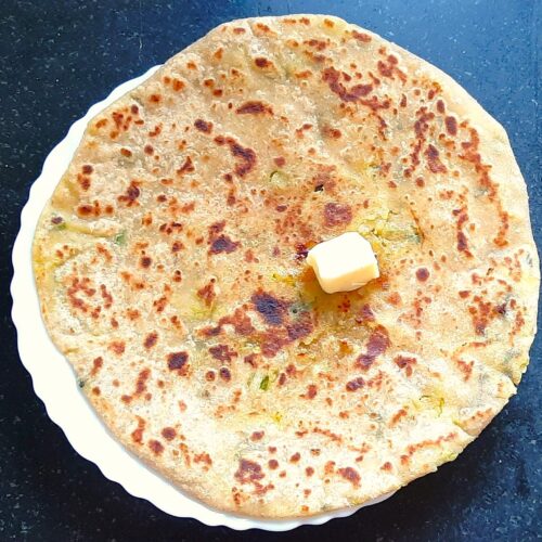 Hot aloo paratha, freshly prepared, is served on a plate with melting butter on the top.