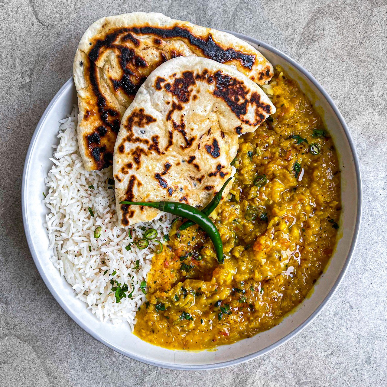 Masoor dal tadka is served in a white bowl with rice and two half chapatis.