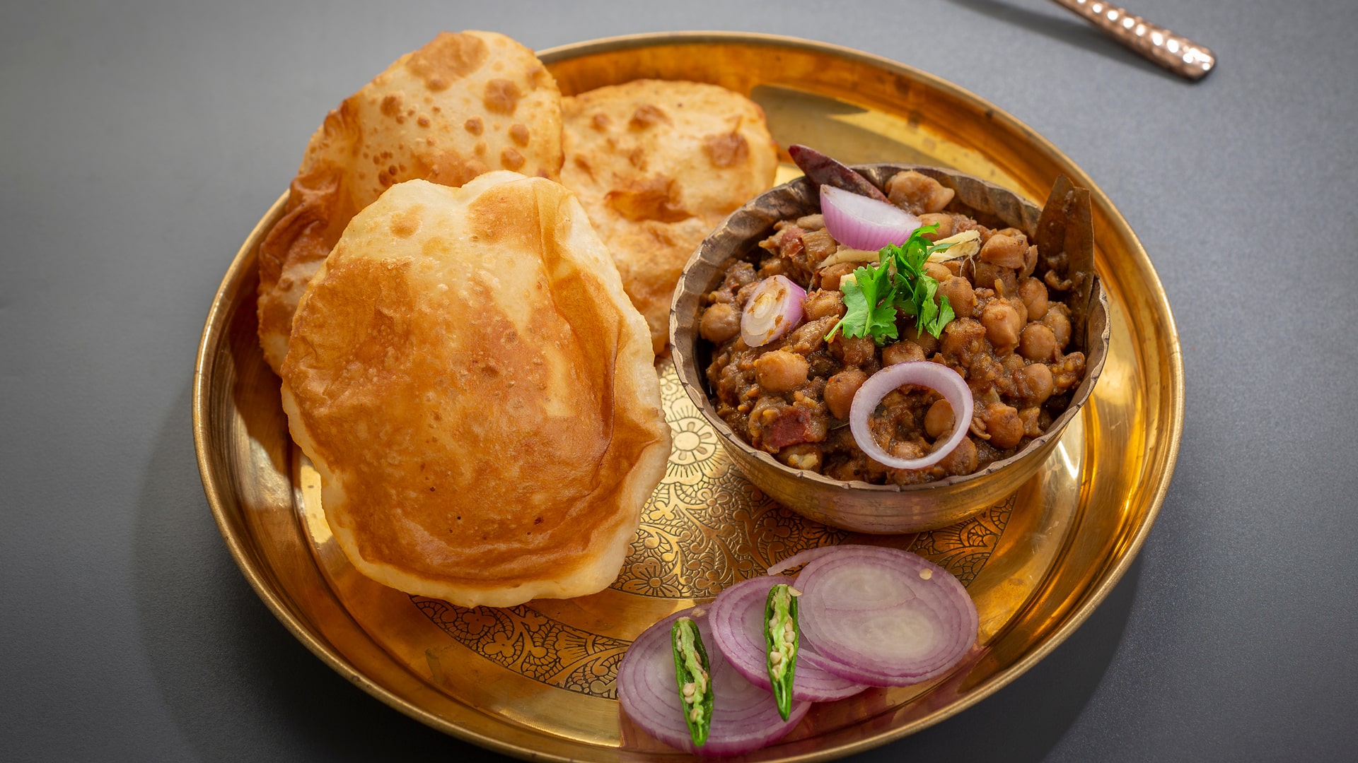 Popular Punjabi dish chole bhature served hot on a golden plate and bowl with green chilli and onion.