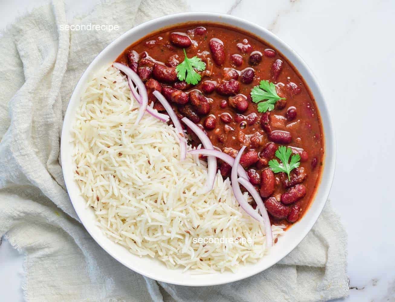 Rajma rice and basmati chawal evenly distributed in a bowl garnished with onions and cilantro.