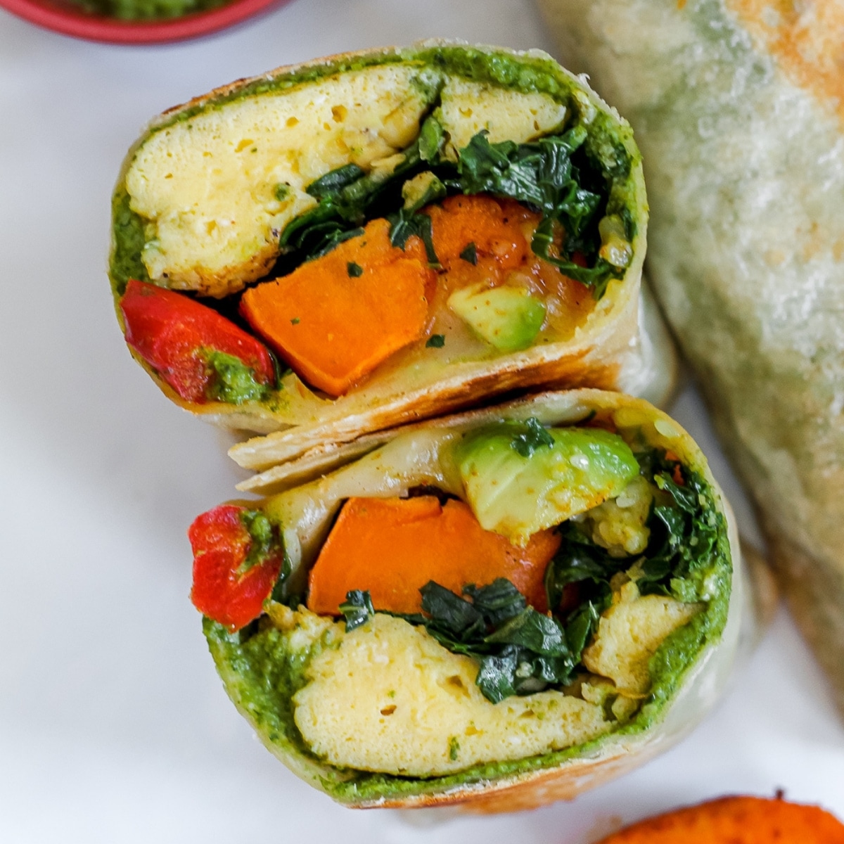 Two rolled pieces of sweet potato breakfast burritos decorated with colourful fillings wrapped nicely and ready to eat.