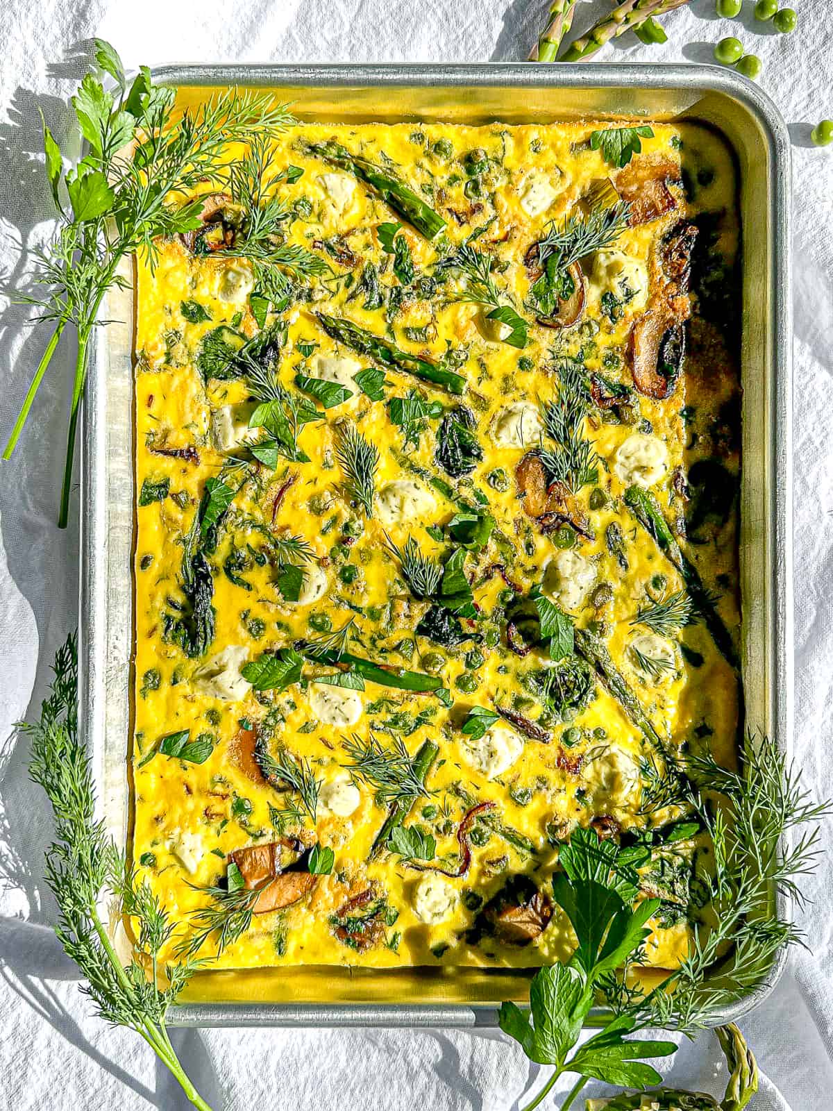 Prepared Sheet Pan Asparagus Frittata garnished with freshly chopped herbs, cut into squares, ready to serve.