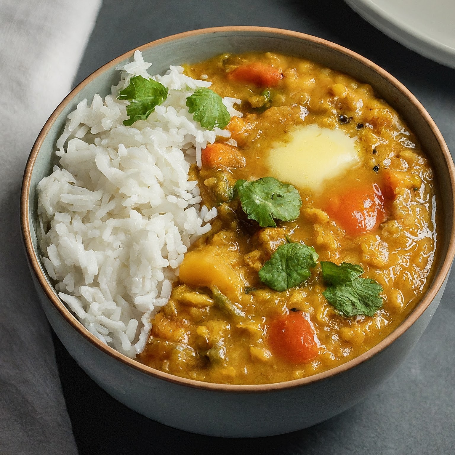 sambhal dal and rice are served in a bowl partinioned well and garnished with green leaved