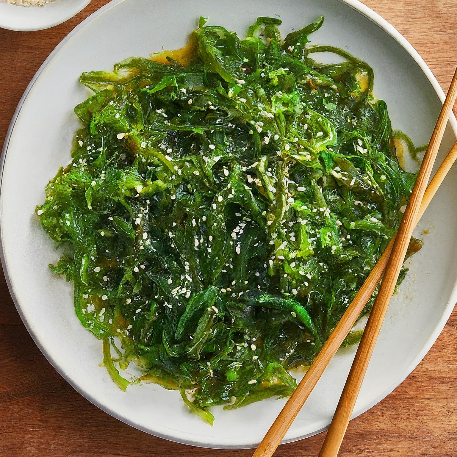 white plate filled with green Japanese seaweed salad besides two chopsticks balanced on the corners