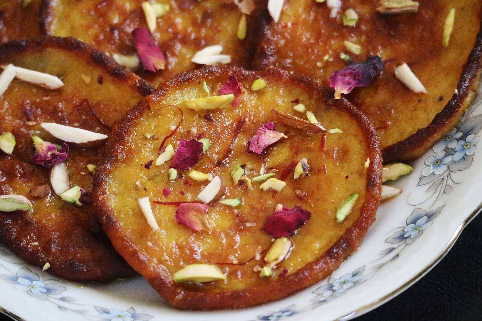 Oiled malpuas garnished with dry fruits are spread in a white plate